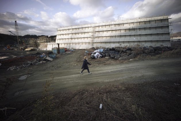 Una mujer camina junto al gigantesco muro de cemento que está siendo erigido frente a la costa en Rikuzentakata, al noreste de Japón, para combatir futuros tsunamis. Foto del 5 de marzo del 2014. Hay quienes piensan que estos muros pueden generar un falso sentido de seguridad y evitar que la gente reaccione en caso de un desastre natural. (AP Photo/Eugene Hoshiko)