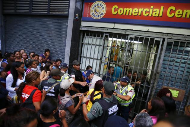 People line up to buy toilet paper and baby diapers as national guards control the access at a supermarket in downtown Caracas January 19, 2015. There's a booming new profession in Venezuela: standing in line. The job usually involves starting before dawn, enduring long hours under the Caribbean sun, dodging or bribing police, and then selling a coveted spot at the front of huge shopping lines. As Venezuela's ailing economy spawns unprecedented shortages of basic goods, panic-buying and a rush to snap up subsidized food, demand is high and the pay is reasonable. Picture taken January 19, 2015. REUTERS/Jorge Silva (VENEZUELA - Tags: POLITICS BUSINESS SOCIETY)