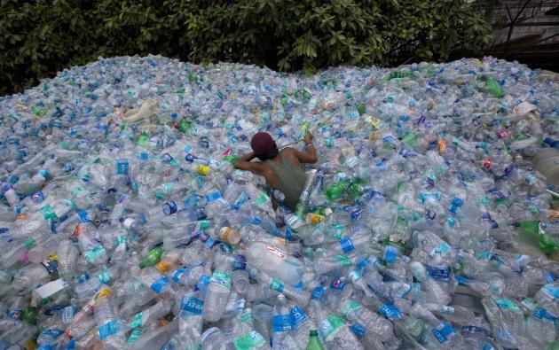A worker uses a rope to move through a pile of empty plastic bottles at a recycling workshop in Mumbai