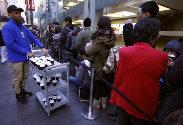 An Apple store employee serves coffee to customers standing in a line on the first day the new iPhone 6 and iPhone 6 Plus went on sale in Sydney