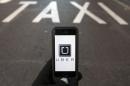 Photo illustration of logo of car-sharing service app Uber on a smartphone over a reserved lane for taxis in a street in Madrid