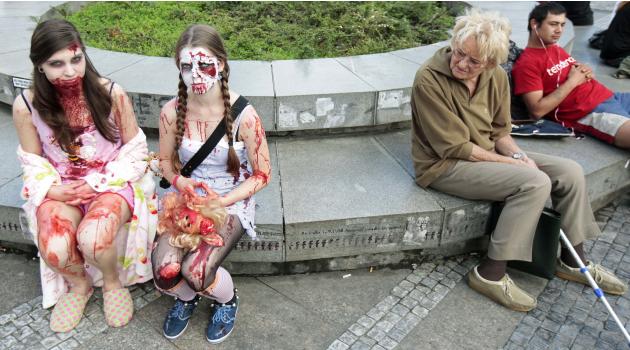 A woman looks at enthusiasts dressed as zombies as they wait for the start of the annual Zombie Walk festival in Prague