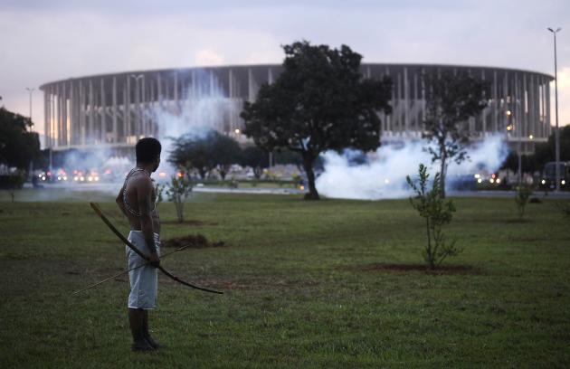 Native Brazilian stands in front of the Mane Garrincha soccer stadium as police use tear gas in Brasilia