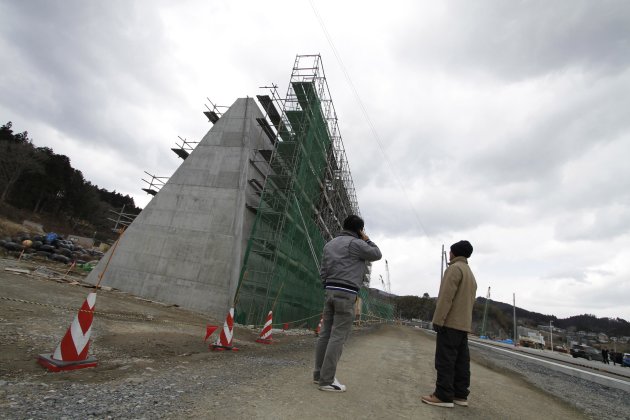 Kazutoshi Musashi (izq) y Shigeru Chiba, ambos residentes del puerto de Osabe, en el noreste de Japón, observan el muro de cemento que está siendo construido para combatir futuros tsunamis. (AP Photo/Koji Ueda)