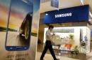 Man using his mobile phone walks past a Samsung   Electronics shop in the company's main office building in central Seou