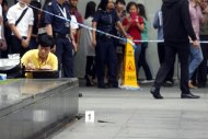 A police investigator (left) collects evidence from the crime scene following a stabbing at the Raffles financial district in Singapore, on November 14, 2014