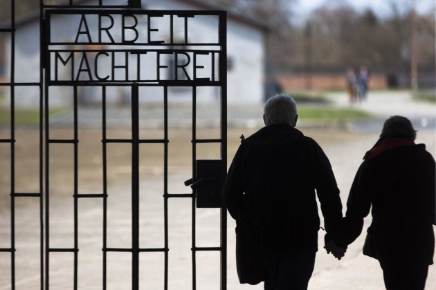 File- In this Jan. 27, 2012, file photo, a couple walks past the slogan 'Arbeit Macht Frei' (Work Sets You Free) at the main entrance of the Sachsenhausen Nazi concentration camp on the international Holocaust remembrance day in Oranienburg, Germany. An Associated Press investigation found dozens of suspected Nazi war criminals and SS guards collected millions of dollars in Social Security payments after being forced out of the United States. (AP Photo/Markus Schreiber,File)