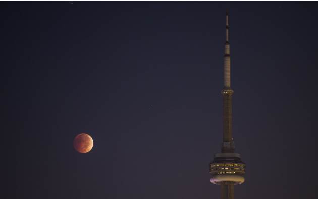 The moon turns orange during a total lunar eclipse behind the CN Tower during moonset in Toronto