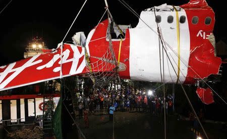 People watch as a section of the tail of  AirAsia QZ8501 passenger plane is lifted off a ship and onto the back of a truck, the day after it was lifted from the seabed, in Kumai Port, near Pangkalan Bun