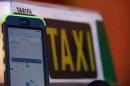 A photo illustration car-sharing service app Uber on   a smartphone next to a taxi sign in Madrid