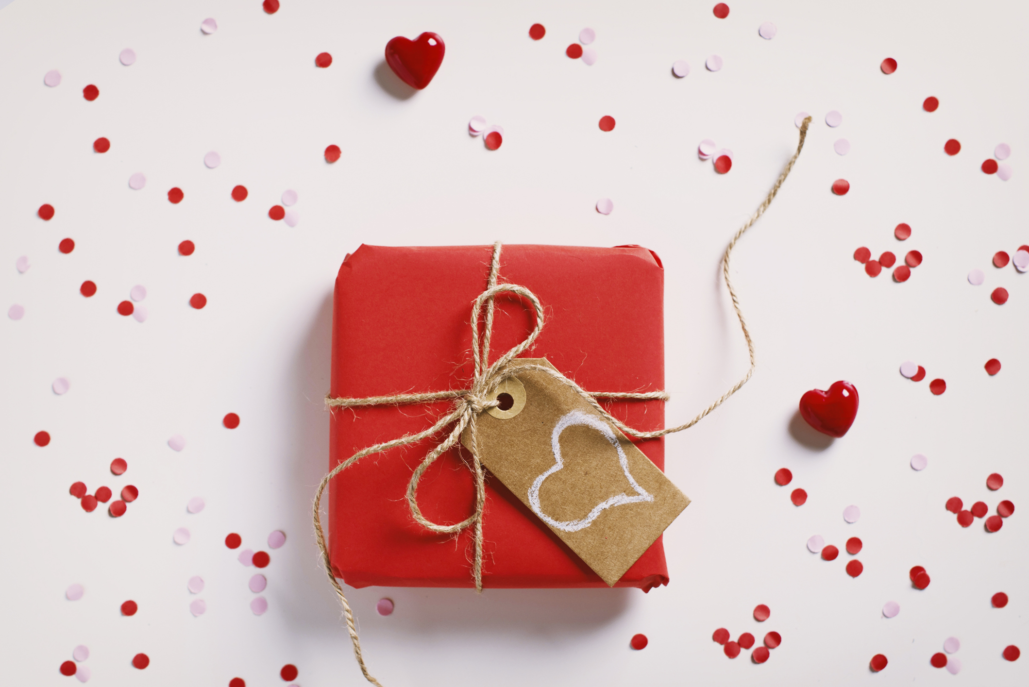 Red gift wrapped with twine with a heart-shaped tag on it.