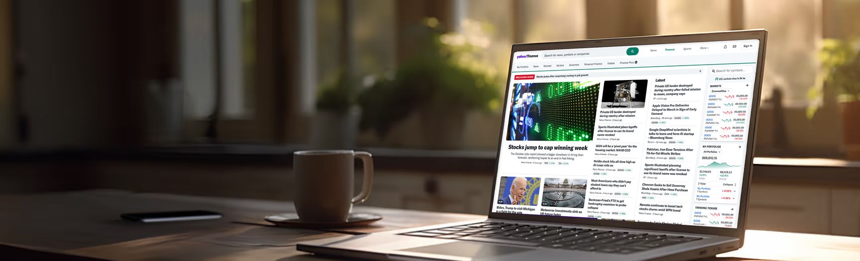 A laptop on a desk next to a cup of coffee. The laptop screen displays the newly revised Yahoo Finance Home Page