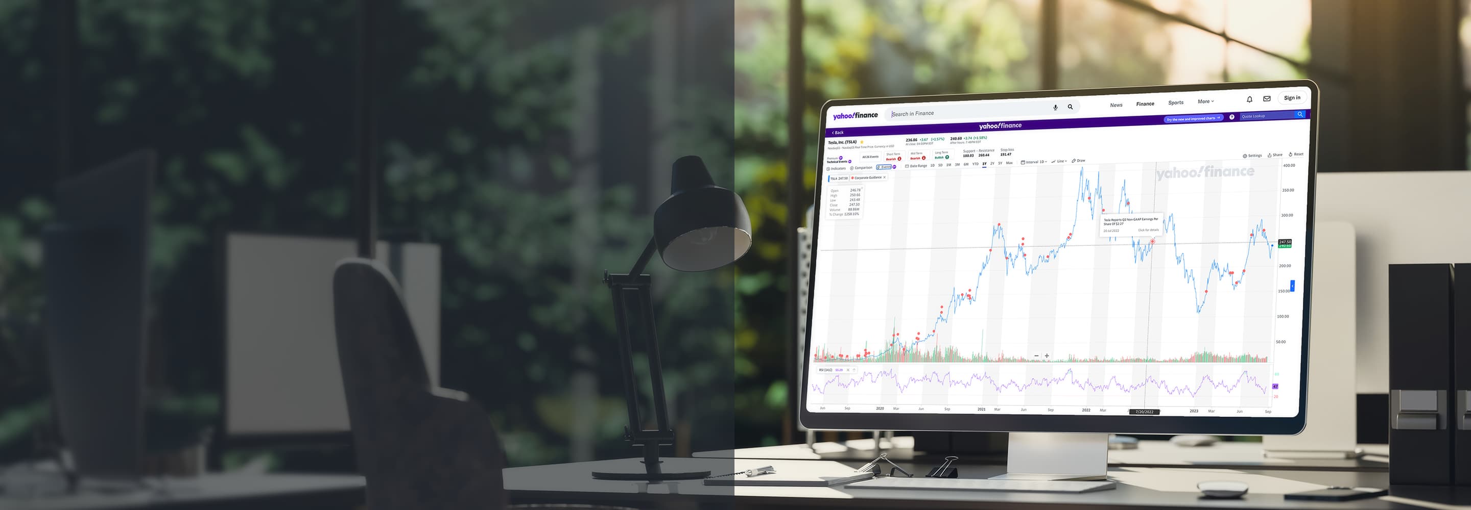 A computer sitting on a desk with a glass window and a lush scene in the background displaying Yahoo Finance charts