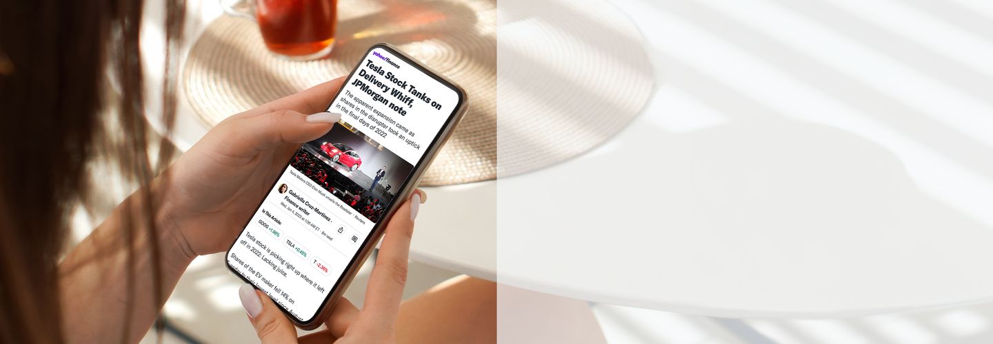 A woman’s hands holding a touch-screen phone with Yahoo Finance news coverage on the screen.