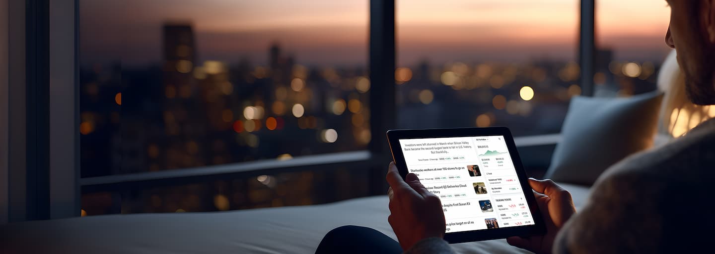 A man sitting overlooking an evening city sky-scape holding an tablet with Yahoo Finance on the screen.