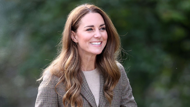 Kate Middleton is seen smiling in a brown tweed coat with her long hair down around her shoulders