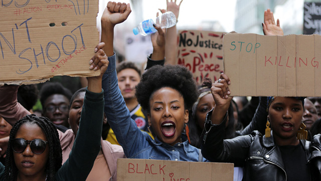 A group of people is seen shouting exuberantly and holding signs with slogans related to the Black Lives Matter movement