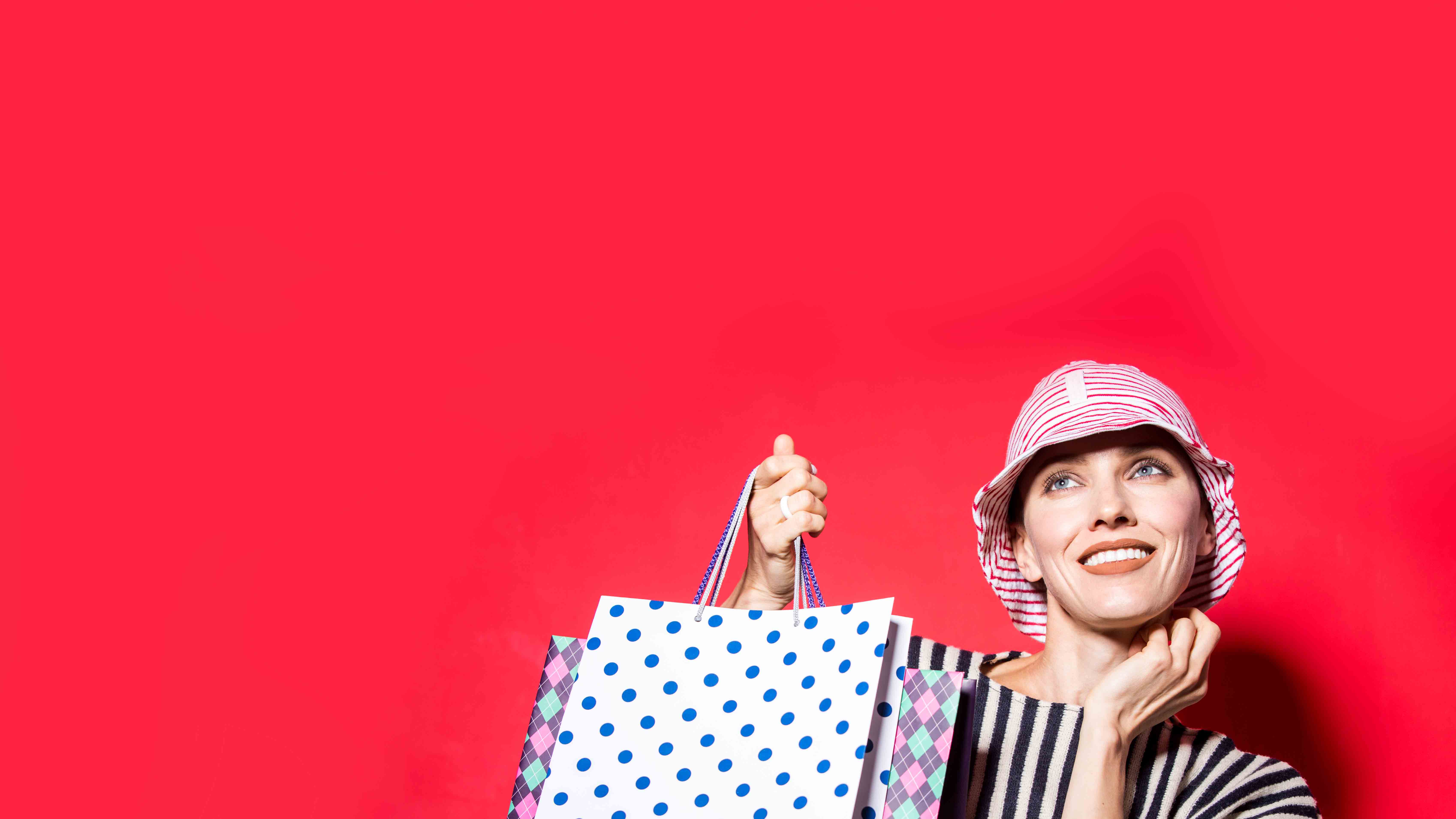 4th of July sale image of woman in red striped hat holding shopping bags. 