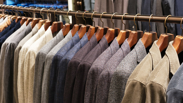 Rows of suits hanging on gold hangers are seen up close on a clothing rack.