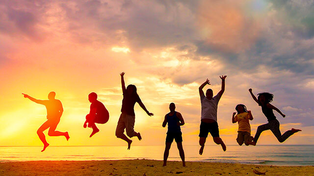 People jumping on a beach against sunset