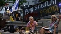 Protesters lie on the ground covered in red paint, as another wears a mask depicting Israeli Prime Minister Benjamin Netanyahu sitting near a paddling pool filled with fake blood, during an anti-government rally in Tel Aviv