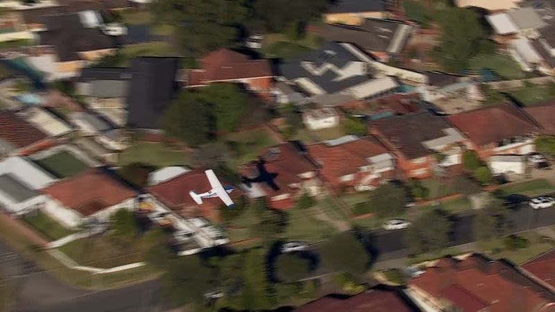 Small plane loses power and skims suburban rooftops before making safe crash landing on belly