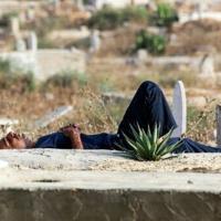 A man sleeps next to tombstones and grave markers at a cemetery in central Gaza's Deir al-Balah