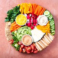 This board caters to plant-based or vegetarian diets. It includes items like vegan or vegetarian deli slices, plant-based cheeses, fresh and dried fruits, raw vegetables, various dips (hummus, guacamole), and a variety of nuts and seeds.