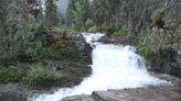 Tourist spotted playing with baby on wet rocks above Glacier National Park waterfall