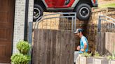 Jeep suspends between house and wall