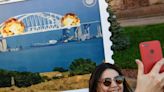 Ukrainians are posing with a giant postage stamp depicting the blown up bridge linking Russia and Crimea