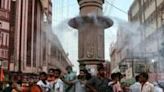 People stand below a water sprinkler installed on a pillar to cool off at a marketplace amid a heatwave in Varanasi, India
