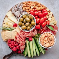 This board takes inspiration from Mediterranean cuisine. It includes items like Mediterranean-style cured meats, such as Serrano ham or capicola, alongside feta cheese, marinated olives, sun-dried tomatoes, hummus, and pita bread.