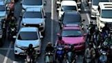 Motorcyclists wait under the shade at a traffic intersection in Bangkok