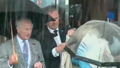 Camilla struggles to get her coat on while battling wind and rain