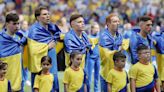 Los jugadores ucranianos, arropados por la bandera de su país a su salida al campo