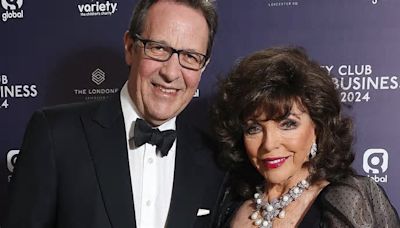 Dame Joan Collins looks glamorous in a black satin dress with semi-sheer puff sleeves as she poses alongside her beloved husband Percy Gibson at Variety Club Showbusiness Awards