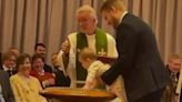 Cheeky toddler splashes water around as priest tries to baptise her
