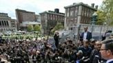 US Speaker of the House Mike Johnson, holding a piece of paper, speaks at Columbia University, with the student pro-Palestinian protest encampment seen in the background