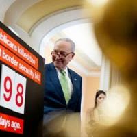 Senate Majority Leader Chuck Schumer stands next to a poster that reads "Republicans killed the toughest border security bill 98 days ago. Democrats are ready to act"