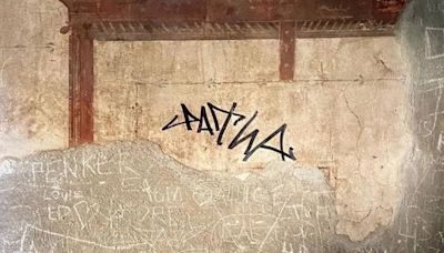 Un turista 'grafitea' la pared de una casa con frescos de hace varios siglos en la antigua ciudad de Herculano (Italia)