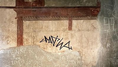 Un turista garabatea su firma con rotulador en una pared con frescos en la antigua Herculano