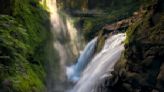 Tourist leads small child onto cliff above raging waterfall at Olympic National Park