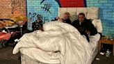 Man and pregnant woman living in a bed next to busy roundabout