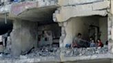 A Palestinian man and his children sit in a destroyed room following the targeting or a residential building by an Israeli air strike in Rafah