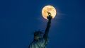 Flower Moon shines behind Statue of Liberty