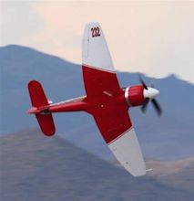 a small red and white plane flying in the sky with mountains in the ...