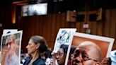 Zipporah Kuria (C) becomes emotional as she holds a photograph of her father Joseph Kuria Waithaka standing next to other family members of those killed in the 2018 and 2019 clashes