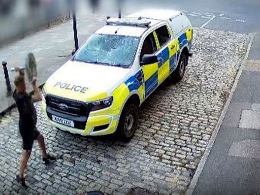 Watch the moment far-right yob throws concrete parasol stand at police car