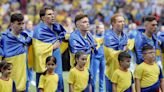 Los jugadores ucranianos, arropados por la bandera de su país a su salida al campo